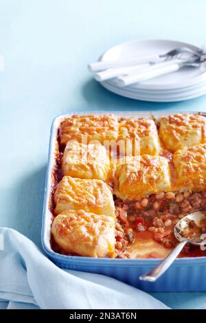Cocotte de haricots avec garniture de biscuit au cheddar sur fond bleu Banque D'Images