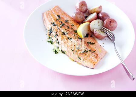 Filet de truite au beurre aux herbes de citron et pommes de terre de bébé sur fond rose Banque D'Images