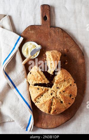 Pain de soda irlandais aux raisins de Corinthe et un petit plat de beurre sur une planche à découper en bois Banque D'Images