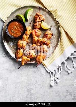 Brochettes de poulet avec sauce trempée et quartiers de lime sur un plateau métallique en tissu rayé Banque D'Images