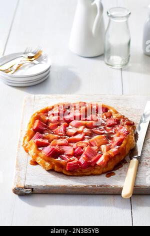 Rhubarb tartelez la tatine sur une planche à découper avec un couteau de service et des assiettes blanches Banque D'Images