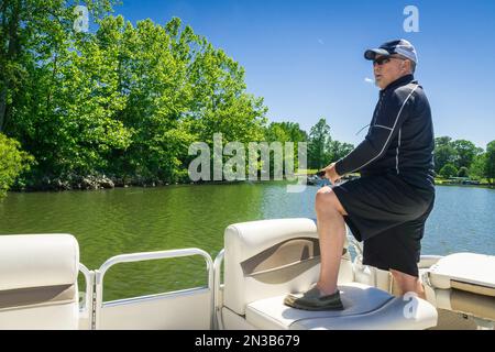 Homme pêchant à partir d'un bateau tout en étant debout sur une journée ensoleillée. Banque D'Images