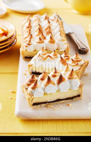 Tarte à la meringue au citron avec une couche de caramel au chocolat coupée en morceaux sur la planche à découper Banque D'Images