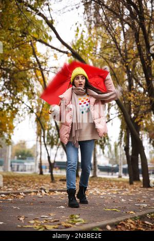 Femme avec parapluie rouge pris dans la rafale de vent à l'extérieur Banque D'Images