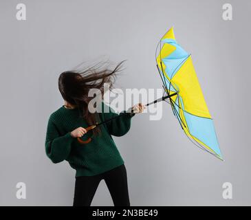 Femme avec parapluie pris dans la rafale de vent sur fond gris Banque D'Images
