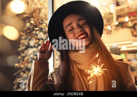 Femme dans des vêtements chauds tenant un sparkler brûlant sur un arrière-plan flou Banque D'Images