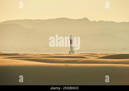 Phare avec une bande rouge sur les dunes de sable ondulées dans la lumière du soir au coucher du soleil, Delta de l'Èbre ; Catalogne, Espagne Banque D'Images