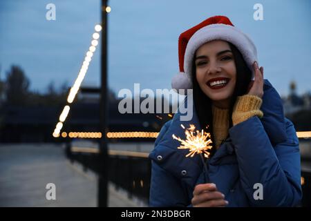 Femme en chapeau de Santa tenant le feu de pargne à l'extérieur, espace pour le texte Banque D'Images