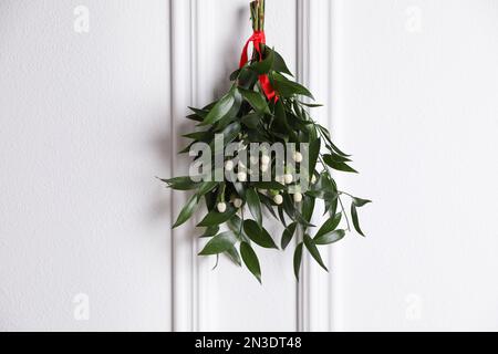 Bouquet de GUI avec ruban rouge suspendu sur fond clair. Décoration de Noël traditionnelle Banque D'Images