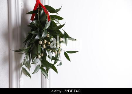 Bouquet de GUI avec ruban rouge suspendu sur fond clair, espace pour le texte. Décoration de Noël traditionnelle Banque D'Images