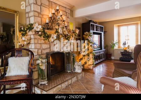 Bois antique et deux fauteuils rembourrés devant la cheminée à bois en pierre taillée naturelle avec décorations de Noël dans le salon. Banque D'Images