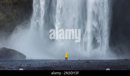 Un touriste solitaire se tient devant l'impressionnante cascade de Skogafoss en Islande alors qu'ils se préparent à prendre une photo ; Skogafoss, Islande Banque D'Images