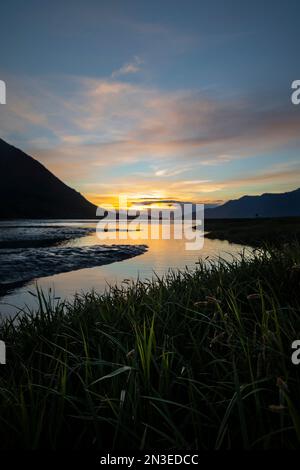 Marais herbeux le long de la rive de Resurrection Creek avec des pentes de montagne silhouetées tandis que le soleil se couche avec une lueur dorée Banque D'Images