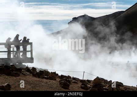 Les personnes se tenant sur la plate-forme d'observation surplombant et prenant des photos du lac Myvatn, entouré par la vapeur qui s'élève des évents géothermiques. L... Banque D'Images