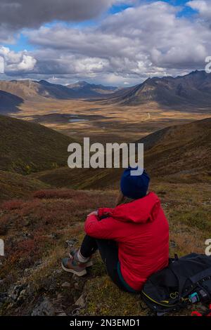 Femme assise sur une montagne au-dessus de la route Dempster profitant du paysage dans le Yukon du Canada ; Yukon, Canada Banque D'Images
