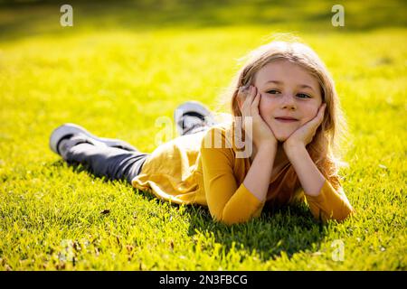 Jeune fille allongée et reposant sur l'herbe lors d'une chaude journée d'automne dans un parc de la ville ; agréments Albert, Alberta, Canada Banque D'Images