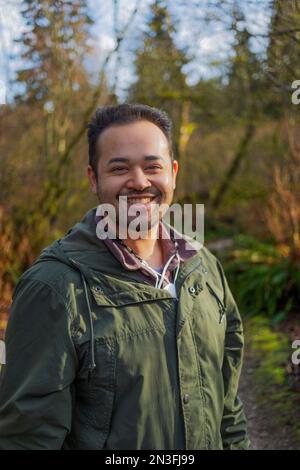 Portrait extérieur d'un jeune homme debout sur un sentier dans une forêt aux couleurs automnales, Green Timbers Urban Forest Park; Surrey, Colombie-Britannique, Canada Banque D'Images