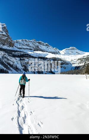 Les femmes raquette et brisent un sentier sur un lac enneigé intact avec des montagnes Rocheuses enneigées dans le parc national Banff Banque D'Images