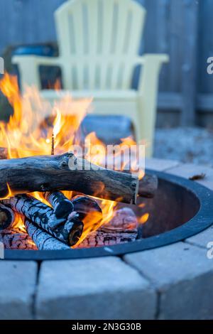 Plan vertical d'une fosse de feu de pierre le jour de l'automne avec une chaise de jardin jaune dans le fond flou Banque D'Images