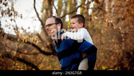 Un père jouant avec son jeune fils qui est pigeback à cheval pendant une sortie familiale dans un parc de la ville pendant la saison d'automne; St. Albert, Alberta, Canada Banque D'Images