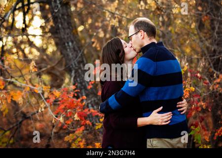 Un couple marié mature s'embrasse tout en passant du temps ensemble à l'extérieur dans un parc de la ville pendant la saison d'automne; St. Albert, Alberta, Canada Banque D'Images