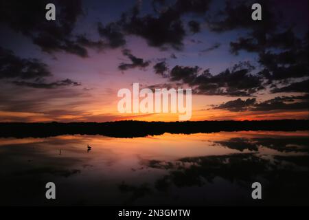 Soleil couchant chaud lumière et nuages sombres se reflètent sur l'eau tranquille avec un rivage silhouette au loin ; Floride, États-Unis d'Amérique Banque D'Images