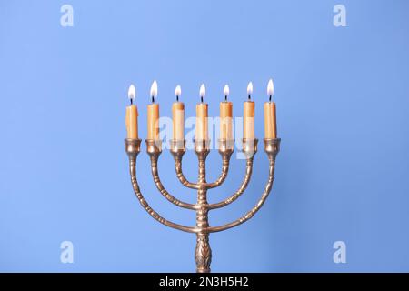 Menorah dorée avec bougies allumées sur fond bleu clair Banque D'Images