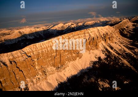 Vue aérienne sur le Rocky Mountain Front du Montana, avec des sommets enneigés des montagnes Rocheuses illuminés par la lumière du coucher du soleil au-dessus des nuages Banque D'Images