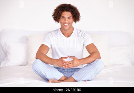 Se concentrer sur le calme. Studio photo d'un jeune homme ethnique élégant, assis à pieds croisés sur un lit et méditant. Banque D'Images