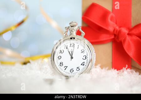 Montre de poche et cadeau sur la neige contre les lumières floues. Compte à rebours du nouvel an Banque D'Images