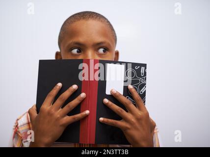 Se cacher derrière son livre. Un jeune garçon qui fait la lecture préparée à l'avant de la classe. Banque D'Images