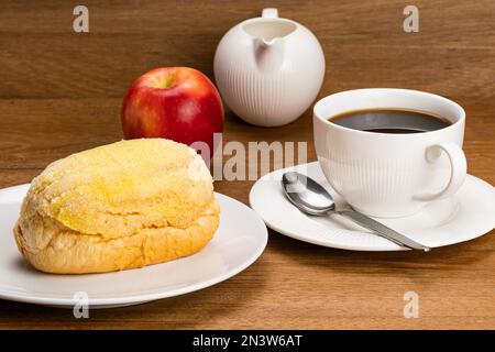 Pain au beurre frais dans une assiette en céramique blanche, une tasse de café noir chaud avec une cuillère en métal dans une soucoupe en céramique, une pomme rouge mûre et une casserole de lait blanc sur un Banque D'Images