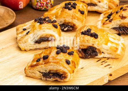 Groupe de pâtisseries danoises avec vue sur le haut et garniture de crème au chocolat avec copeaux de chocolat sur planche à découper en bois avec pomme rouge mûre et Banque D'Images