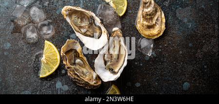 Huîtres fraîches ouvertes servies avec des quartiers de citron et des cubes de glace sur fond de pierre rustique vue de dessus, concept de bar à huîtres de fruits de mer Banque D'Images