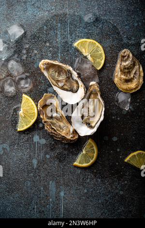 Huîtres fraîches ouvertes servies avec des quartiers de citron et des cubes de glace sur fond de pierre rustique vue de dessus, concept de bar à huîtres de fruits de mer Banque D'Images