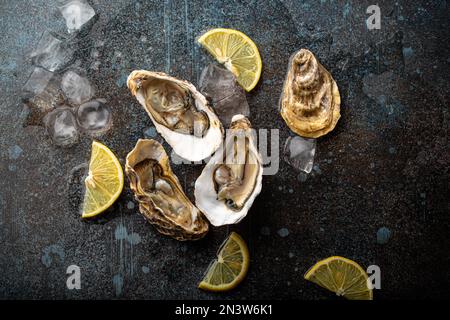 Huîtres fraîches ouvertes servies avec des quartiers de citron et des cubes de glace sur fond de pierre rustique vue de dessus, concept de bar à huîtres de fruits de mer Banque D'Images