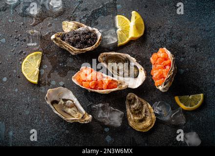 Assortiment de fruits de mer entrées et hors-d'œuvre : huîtres fraîches ouvertes, caviar noir, tartare de saumon servi avec des quartiers de citron et des cubes de glace dessus plan d'eau Banque D'Images