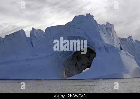 Grand iceberg avec trou, petit bateau devant lui, minuit, été dans l'Arctique, Ilulissat, Disko Bay, Amérique du Nord, Groenland, Danemark Banque D'Images