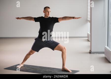 Un homme de construction athlétique fait du yoga dans la salle de gym sur un tapis. Banque D'Images