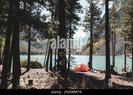 La tente se trouve à côté de choses touristiques sur une corde dans les arbres près du lac alpin Shavlinskoye avec une fille voyageur dans les montagnes. Banque D'Images