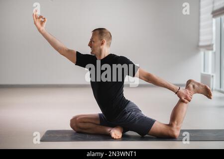 Un homme de construction athlétique fait du yoga dans la salle de gym sur un tapis. Banque D'Images