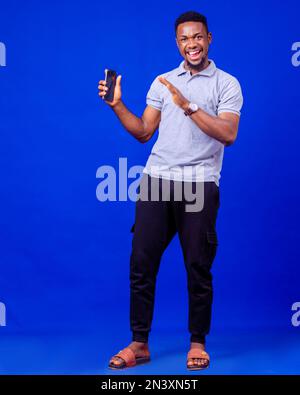 Joyeux homme noir millénaire dans une ambiance décontractée en utilisant un smartphone moderne, en vérifiant les médias sociaux, Banque D'Images