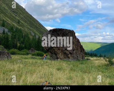 Une fille voyageur avec un sac à dos et un chapeau marche sur des bâtons de randonnée, sur fond d'une grande pierre dans les montagnes de l'Altaï. Banque D'Images