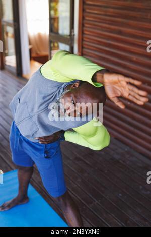 Vue à grand angle de l'homme senior américain d'Afrique chauve qui s'étire les bras et s'exerce dans une cabane en rondins Banque D'Images