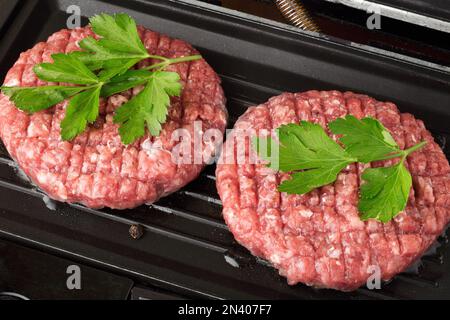 Viande de boeuf haché cru steak côtelettes hamburger frites sur un gril chaud. Côtelette pour hamburger avec légumes et épices. Banque D'Images