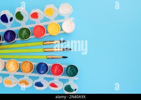 Peintures colorées en pots sur fond bleu près des brosses. Palette de couleurs. Concept-créativité et thème scolaire. Des boîtes ouvertes de peinture gouache sont à proximité Banque D'Images