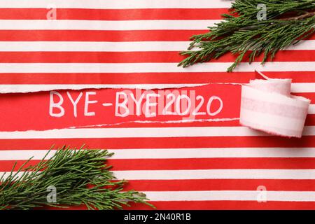 Thuja branches et texte Bye-bye 2020 sur fond rouge, vue à travers le papier déchiré rayé Banque D'Images