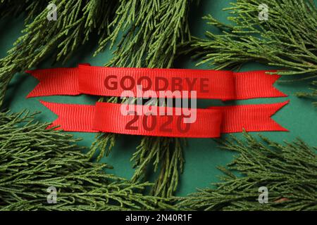 Rubans rouges avec texte Au revoir 2020 et branches de thuja sur fond vert, plat Banque D'Images