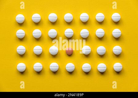Une rangée de pilules médicales blanches et une pilule rouge au milieu sur fond jaune. Banque D'Images