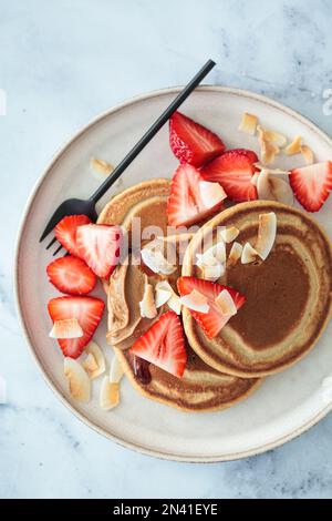 Crêpes végétaliennes avec fraises, beurre de noix, chips de noix de coco et sirop, vue du dessus. Banque D'Images